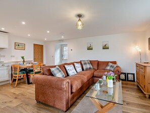 A living room with a brown leather sofa, a glass coffee table, and a dining area with wooden chairs and a white table. - 2 Bed in Ripon (oc-94000) (Littlethorpe)