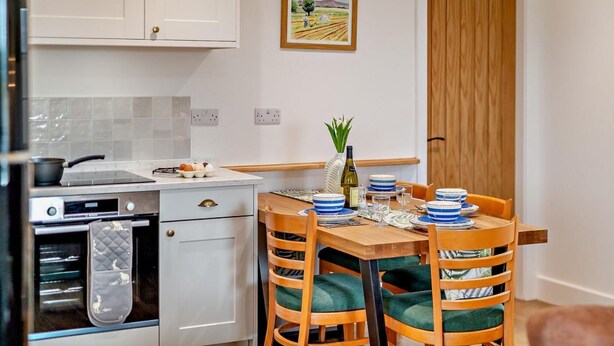 A kitchen with white cabinets, a stove, and a dining table set for four with blue and white plates. - 2 Bed in Ripon (oc-94000) (Littlethorpe)