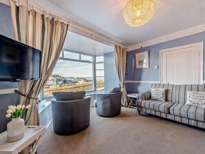 Ein modernes Wohnzimmer mit einem großen Fenster, einem Flachbildfernseher, einer Couch und einer dekorativen Lampe.