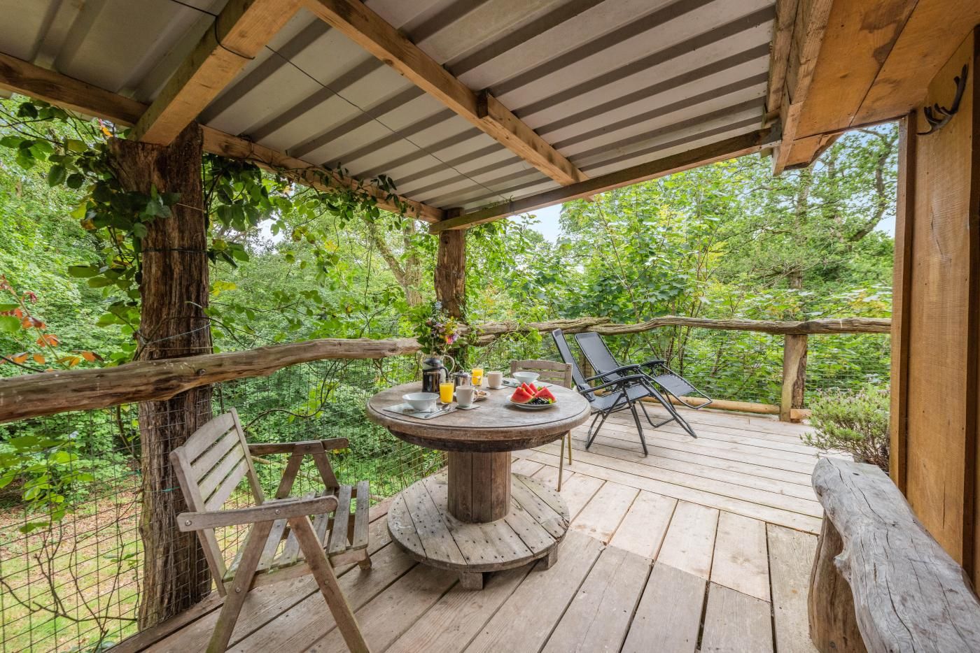 Une terrasse extérieure en bois, avec une table ronde, des chaises et une rambarde rustique.
