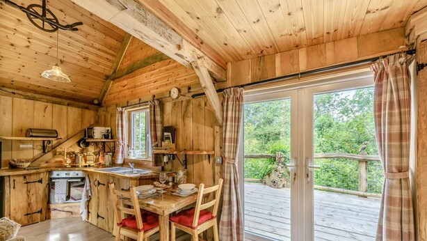 En træhytte med spiseplads, køkken og store skydedøre til en udendørs terrasse.
