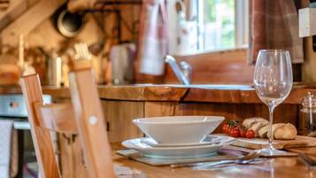 A kitchen with a wooden table, a white bowl, a wine glass, and some bread.