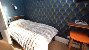 Een kamer met een bed, een klein tafeltje met een tijdschrift, een stoel en een wand met een geometrisch patroon.