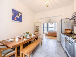 A dining area with a wooden table, benches, and a view of the living room. - 7 Bed in St. Leonards-on-sea (oc-52620) (Hastings)