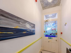 A hallway with a painting on the wall, a door with a fire exit sign, and a ceiling with a decorative pattern. - 7 Bed in St. Leonards-on-sea (oc-52620) (Hastings)