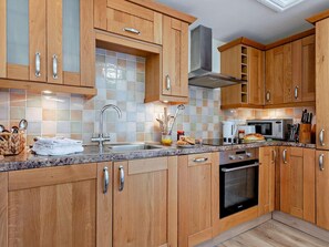 A kitchen with wooden cabinets, a stainless steel sink, a microwave, and a built-in oven. - 1 Bed in Penzance (oc-75689) (Lamorna)