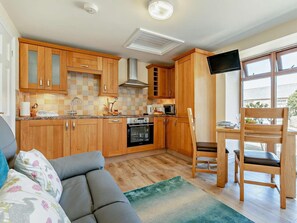 A compact kitchen with wooden cabinets, a built-in oven, and a microwave. - 1 Bed in Penzance (oc-75689) (Lamorna)