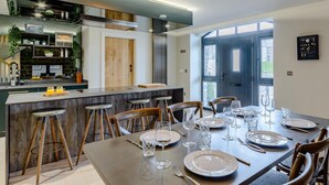 Una cocina moderna con una isla central, taburetes de bar y una mesa de comedor preparada para seis personas, con vasos y platos.