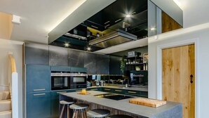 Una cocina moderna con una isla central, taburetes de bar, electrodomésticos integrados y una puerta de madera.