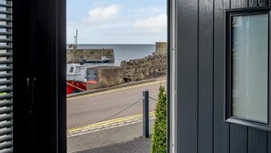 Vista costera desde un edificio con muro de piedra y camino que lleva a un muelle.