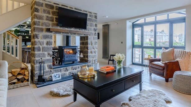 Una sala de estar moderna con chimenea de piedra, televisor de pantalla plana, comedor y ventanas amplias.