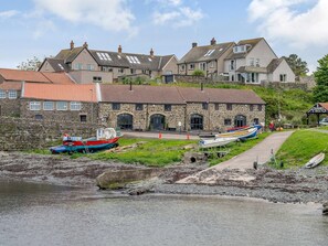 Un bâtiment en pierre avec une façade en pierre, un chemin pavé et des bateaux amarrés au bord de l’eau.