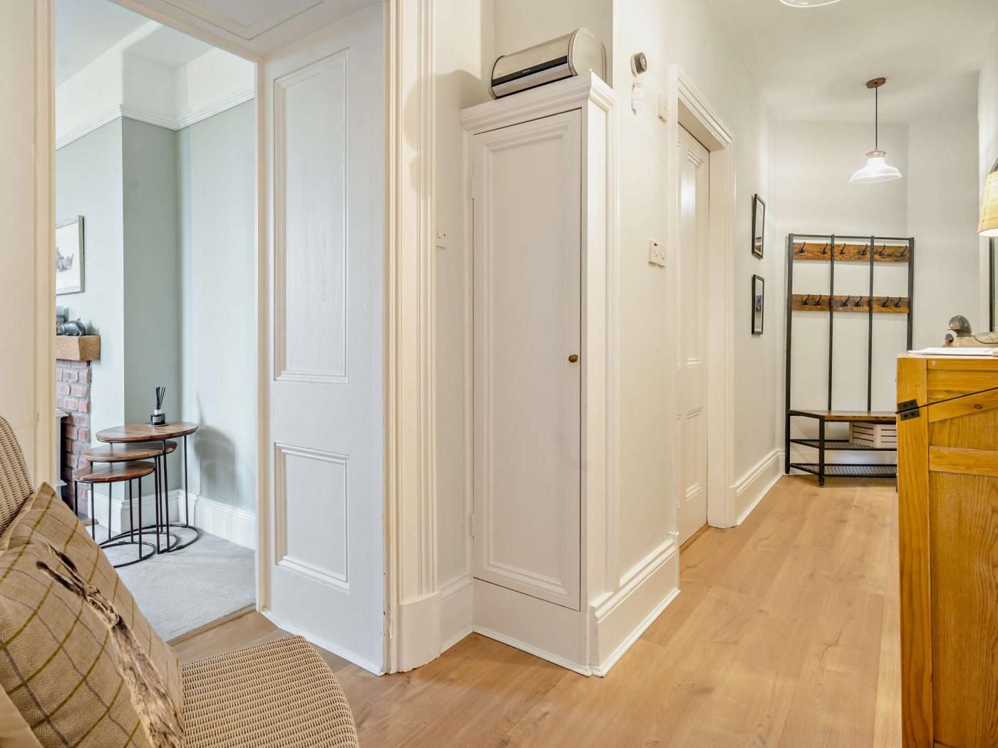 A room with a wooden floor, white walls, a white door, a bench, and a hanging light fixture.