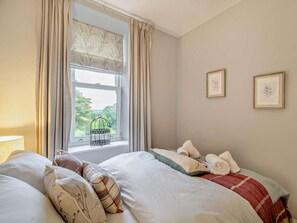 Un dormitorio con cama, almohadas, una ventana con cortinas y una jaula de pájaros.
