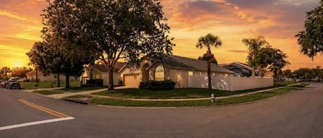 Una calle residencial con casas, cielo despejado y un atardecer.