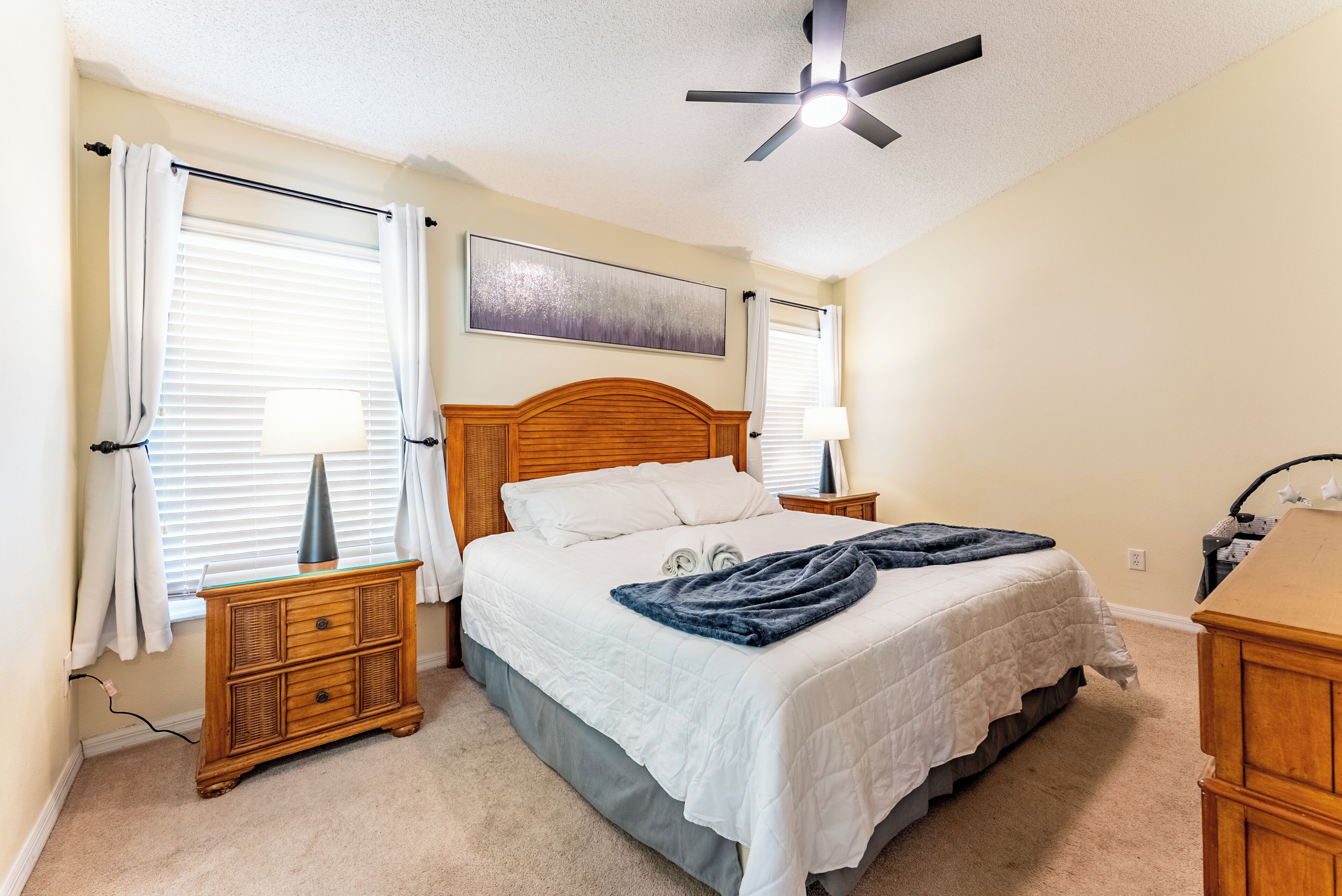 A bedroom with a bed, bedside tables, a ceiling fan, and a window with curtains.