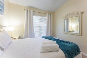 Una habitación de hotel con una cama, una mesita de noche, una lámpara, una ventana con cortinas y un espejo en la pared.