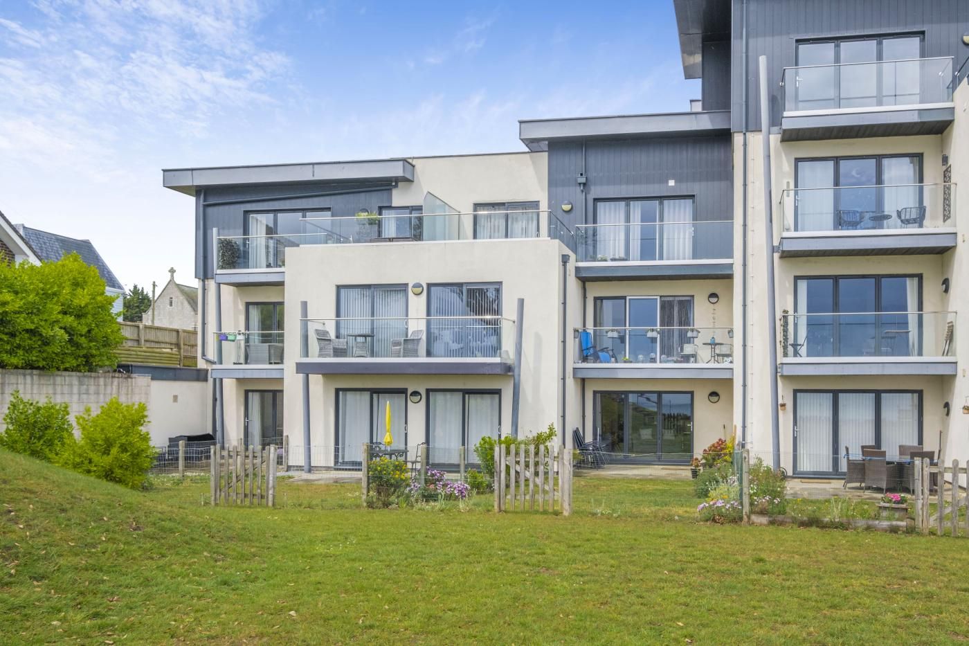 A modern multi-story residential building with balconies, large windows, and a well-maintained lawn.