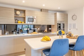 A modern kitchen with a central island, built-in appliances, and a dining area with blue chairs. - 2 Bed in Sandown (oc-90013) (Sandown)
