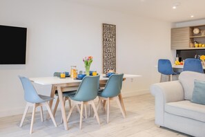 A modern dining area with a white table, blue chairs, and a decorative wall piece. - 2 Bed in Sandown (oc-90013) (Sandown)