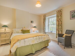 Ein Schlafzimmer mit einem Bett, zwei Nachttischen, einem Sessel, einem Fenster mit Vorhängen und einer Lampe.