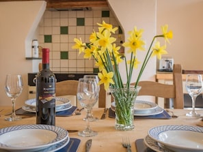 Ein Esstisch ist gedeckt mit Tellern, Besteck, Wein und einer Vase mit gelben Blumen.