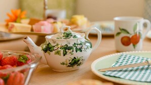 Ein Tisch mit Teekanne, Tasse, Teller mit kariertem Servietten und einer Schale Erdbeeren.