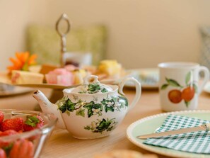 Uma mesa com um bule, uma xícara, um prato com guardanapo quadriculado e uma tigela de morangos.