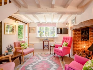 A cozy room with a fireplace, a pink armchair, a wooden table, and a patterned rug. - 2 Bed in Salisbury (oc-88922) (Bodenham)