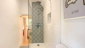 Ein schmales Badezimmer mit gemusterten Fliesen, einer Dusche und einem WC.