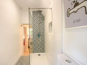 Casa de banho pequena com azulejos estampados, chuveiro e sanita.