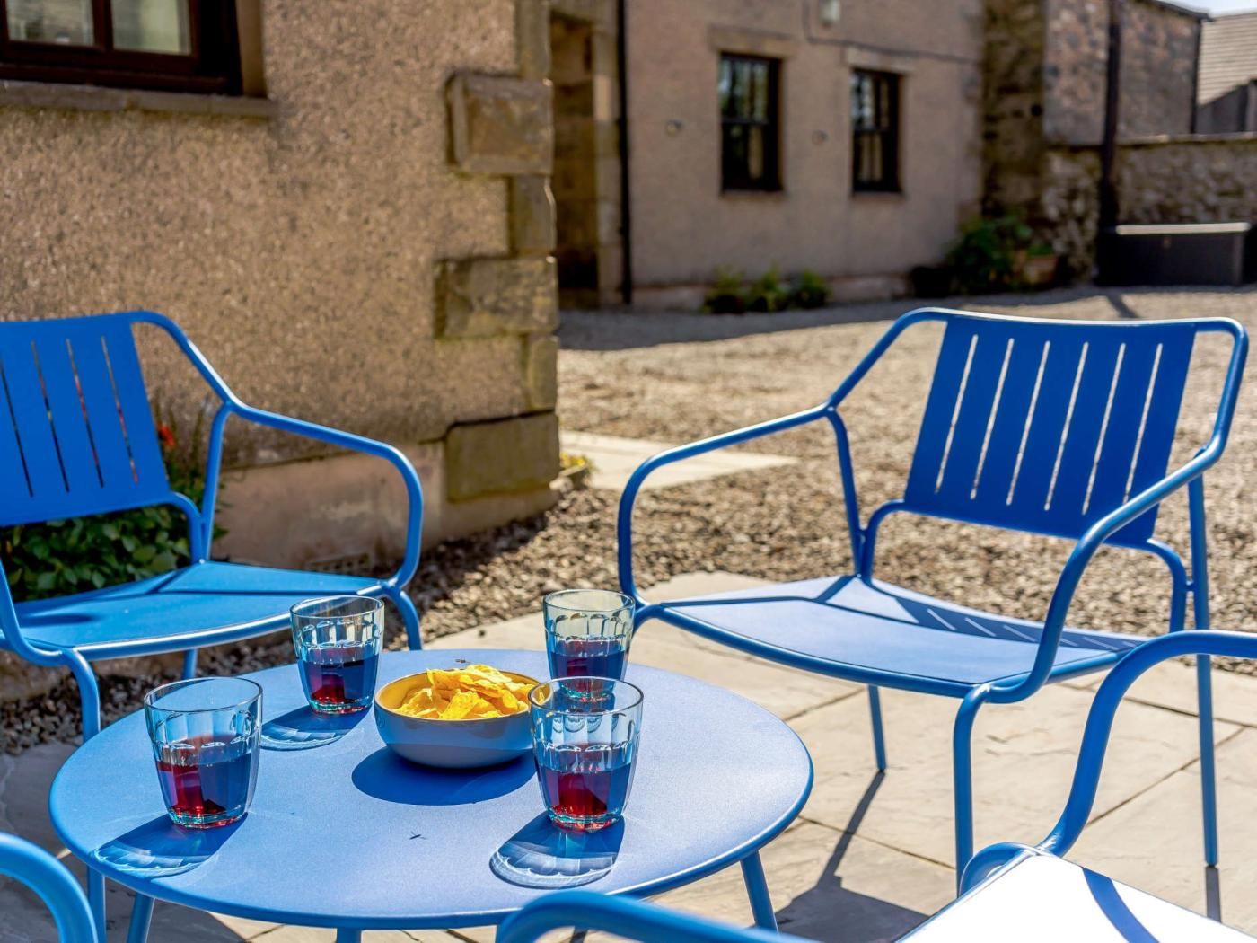 A patio area with blue metal chairs and a table, a bowl of snacks, and several glasses of a blue beverage.