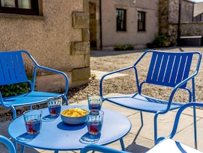 Eine Terrasse mit blauen Metallstühlen und einem Tisch, einer Snackschale sowie mehreren Gläsern eines blauen Getränks.