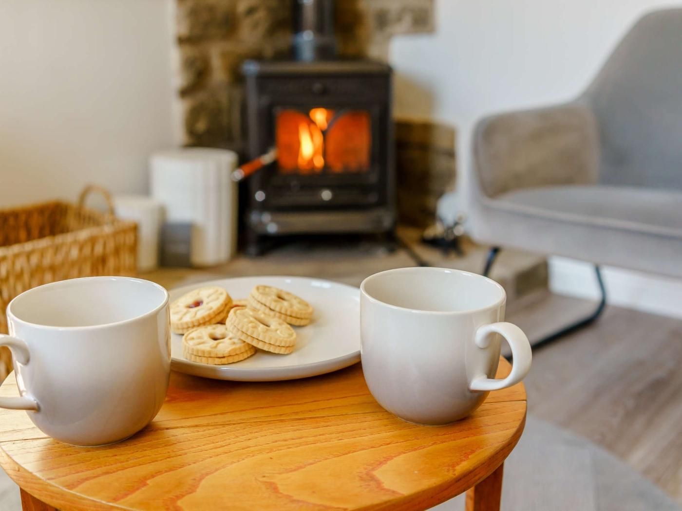 Quarto aconchegante com lareira, um prato de biscoitos e duas canecas em uma pequena mesa de madeira.