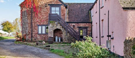 A rustic building with a stone facade, a wooden staircase, and a pink exterior.