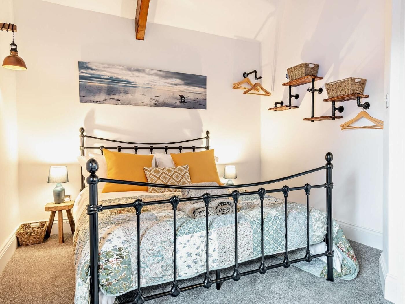 A bedroom with a metal bed frame, a painting of a beach scene, and wall-mounted baskets.