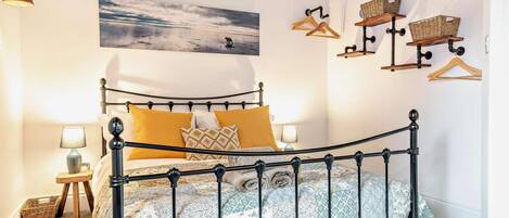 Un dormitorio con estructura de cama metálica, un cuadro de una escena de playa y cestas fijadas a la pared.