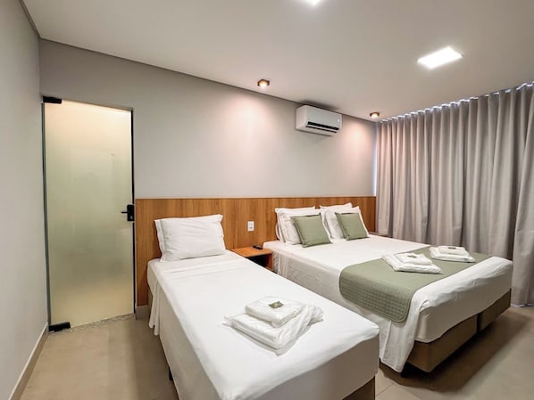 A hotel room with two single beds, a wooden headboard, a nightstand, and a window with curtains.