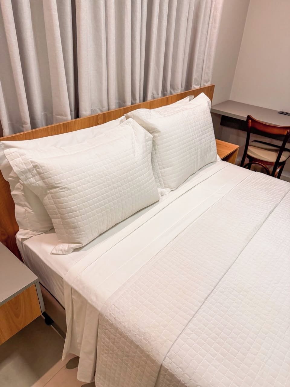 Een bed met een houten hoofdbord, een wit gebogen matras en twee kussens.
