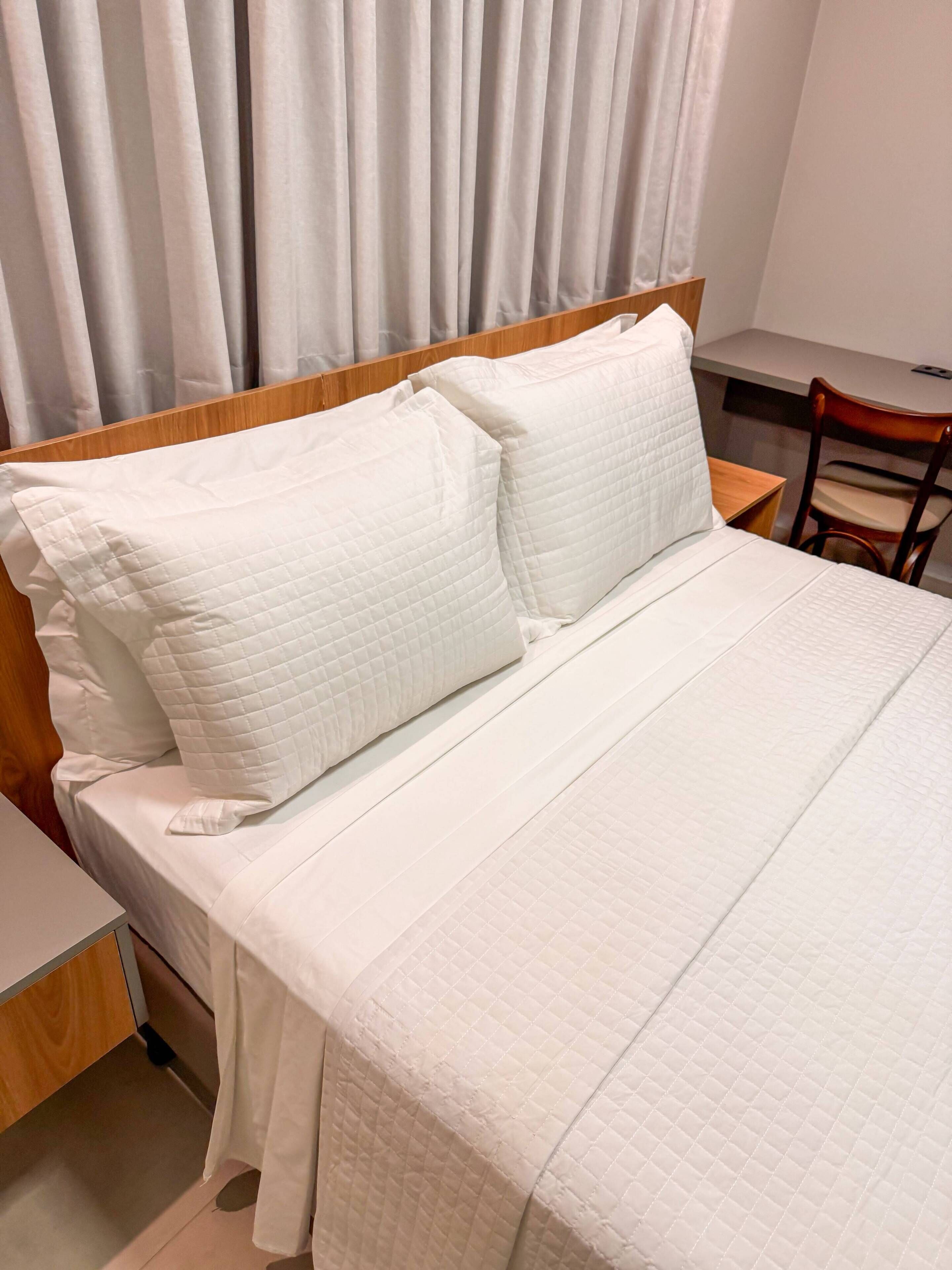 Una cama bien hecha con ropa blanca, un cabecero de madera y una pequeña mesita de noche.