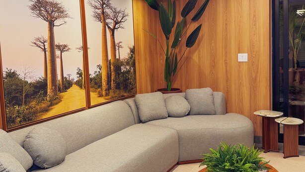 Una sala de estar moderna con un sofá seccional, un cuadro grande de árboles, una planta en maceta y una pequeña mesa de madera.