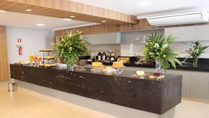 Una moderna recepción con mostrador de mármol, dos grandes plantas en macetas y una estación de café.