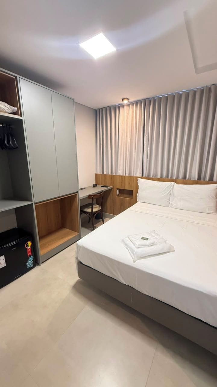 A hotel room with a bed, a desk, a wardrobe, and a curtain.
