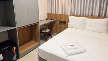 A hotel room with a bed, a desk, a wardrobe, and a curtain.
