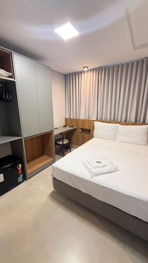 Ein Hotelzimmer mit Bett, Schreibtisch, Kleiderschrank und Vorhang.