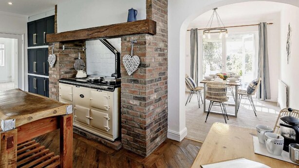 A kitchen with a brick wall, wooden cabinets, and a stove. - 3 Bed in Mablethorpe (oc-sealc) (Mablethorpe and Sutton)
