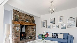 A living room with a brick fireplace, a blue sofa, a white coffee table, and framed artwork on the wall. - 3 Bed in Mablethorpe (oc-sealc) (Mablethorpe and Sutton)