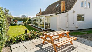 A house with a conservatory, a wooden bench, and a well-maintained garden. - 3 Bed in Mablethorpe (oc-sealc) (Mablethorpe and Sutton)