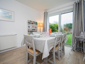 Een eetruimte met een tafel voor vier personen, stoelen, een boekenkast en een raam met gordijnen.