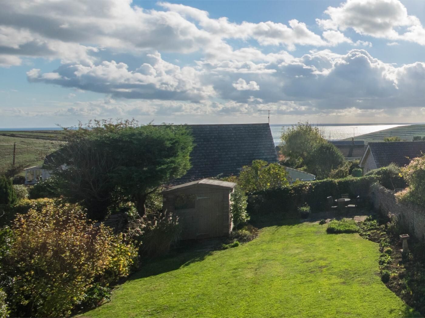 Un paysage rural avec une zone herbeuse, un bâtiment en pierre et une vue sur la mer.